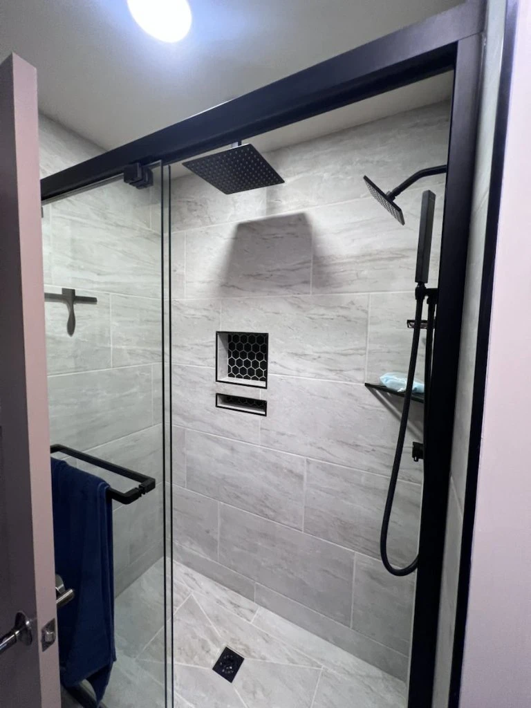 Shower remodel with tile, glass enclosure, niche, black fixtures, and rainfall showerhead in Jacksonville, FL